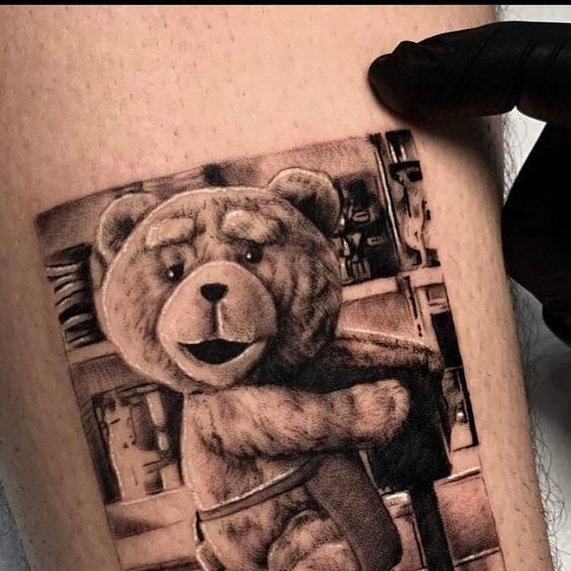 a black and white photo of a teddy bear tattoo on the right thigh, next to a man's leg