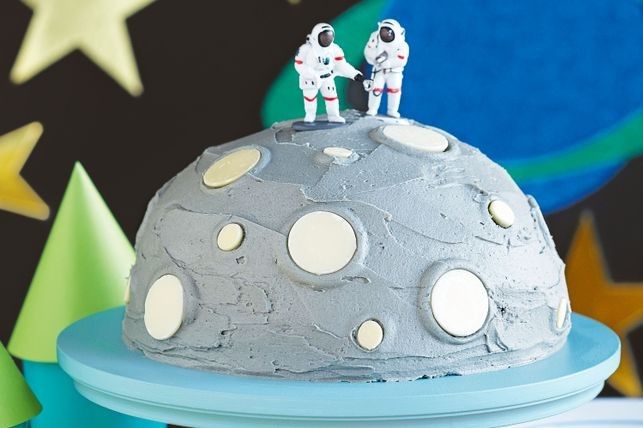 two small toy astronauts are on top of a cake that looks like an outer space base