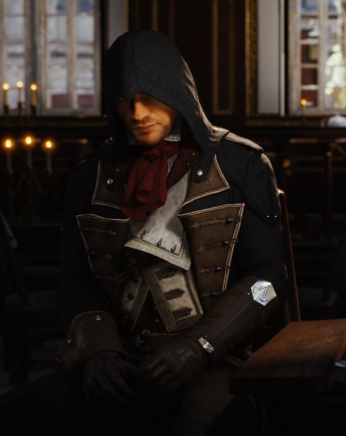 a man dressed in medieval clothing sitting at a table with a candle lit room behind him