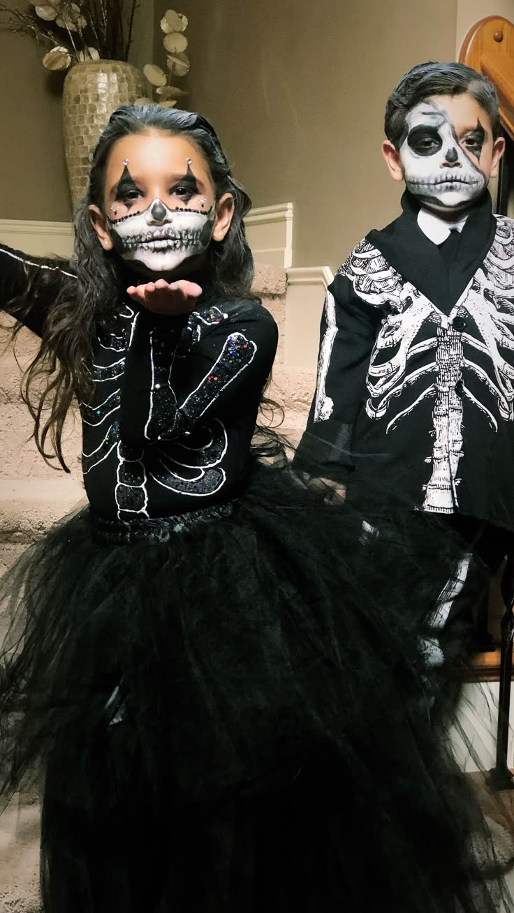 two children dressed up in skeleton makeup and black tutu skirts, sitting on stairs