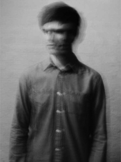 a man standing in front of a wall with his face obscured by the shirt on