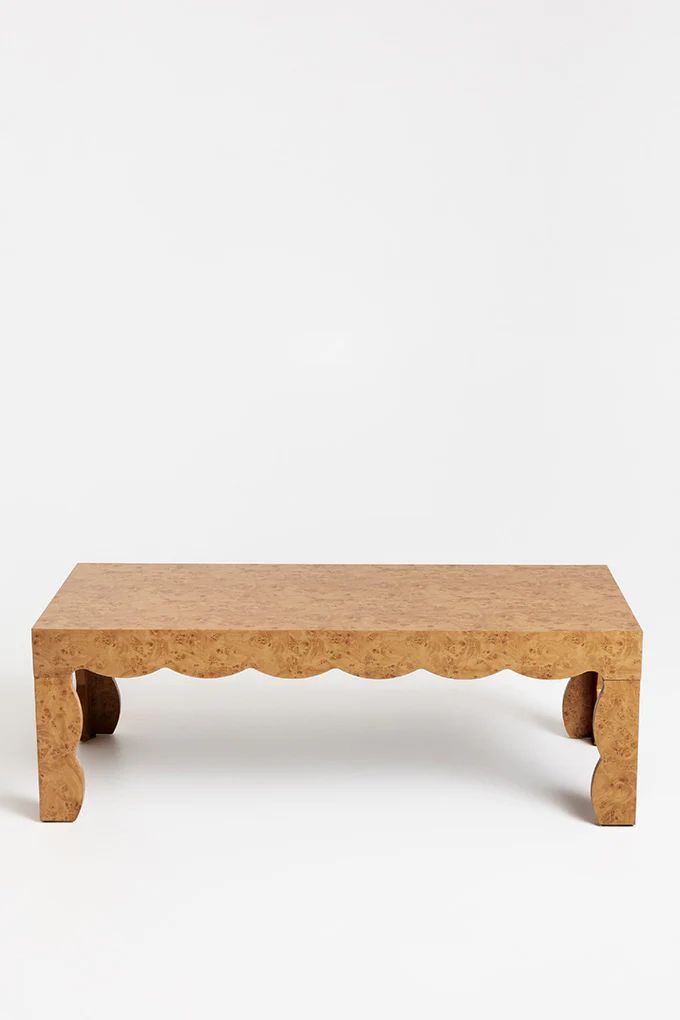 a small wooden bench with scalloped legs on a white background in front of a wall