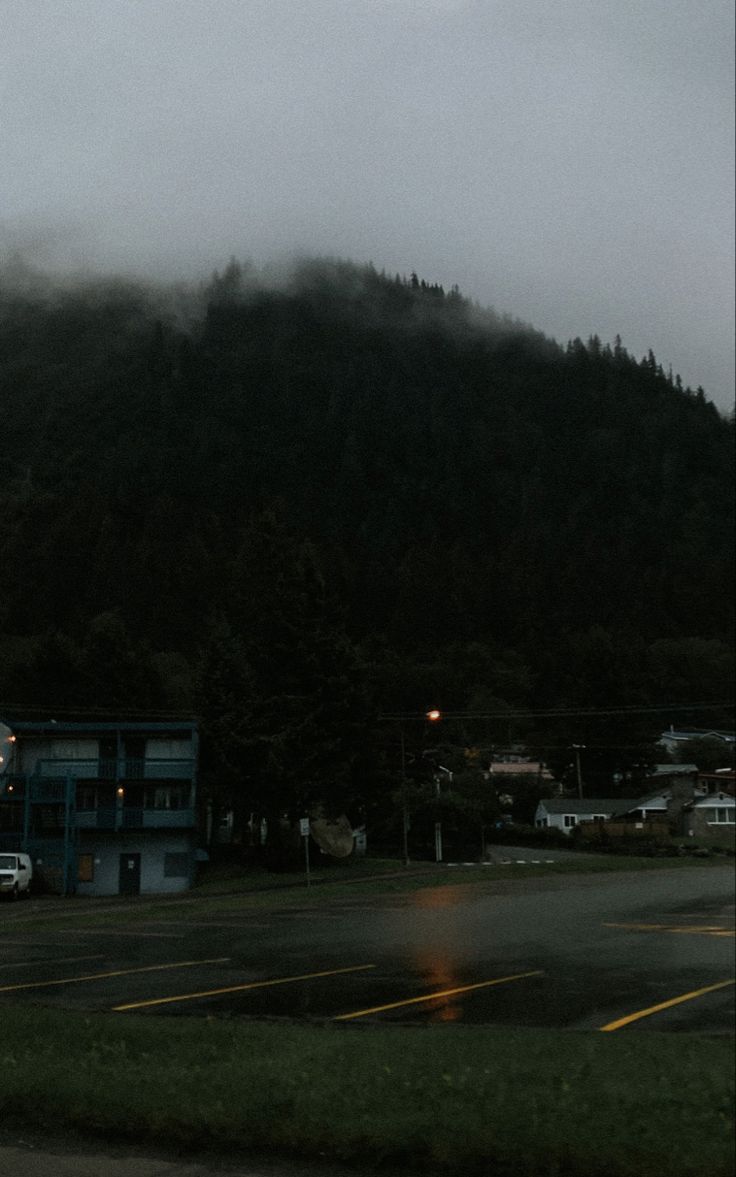 a foggy mountain is in the distance with cars parked on the road below it