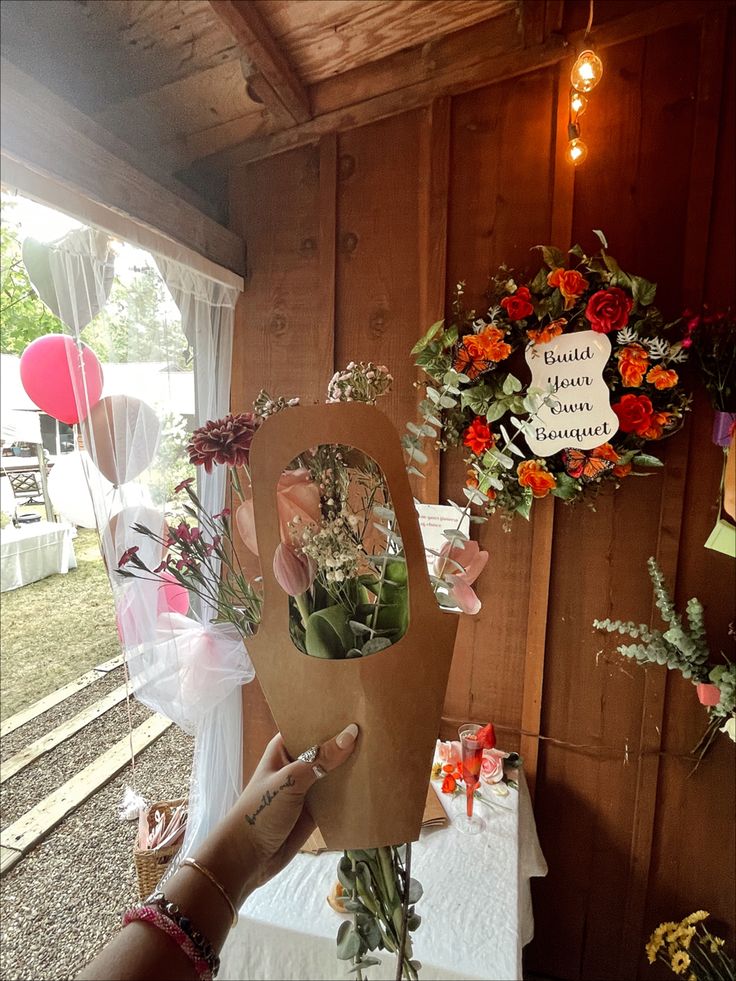 a person holding up a piece of cardboard with flowers on it in front of a wooden wall