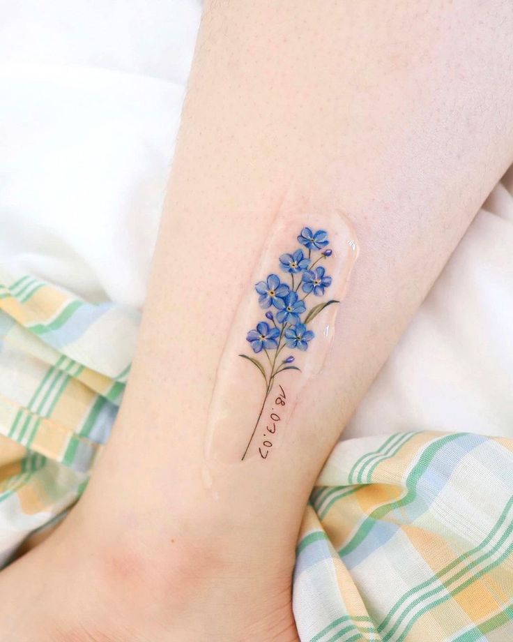 a small blue flower tattoo on the left ankle and right leg, with words written in cursive writing