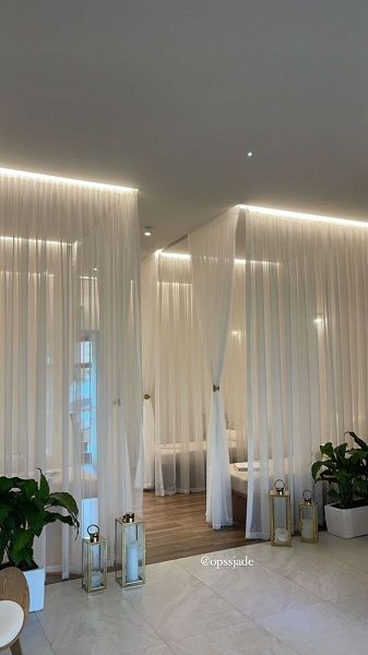 a living room with white drapes and plants in the corner on either side of the window