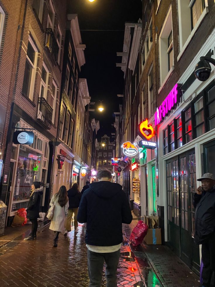 people are walking down the street in an alleyway at night with neon signs on buildings