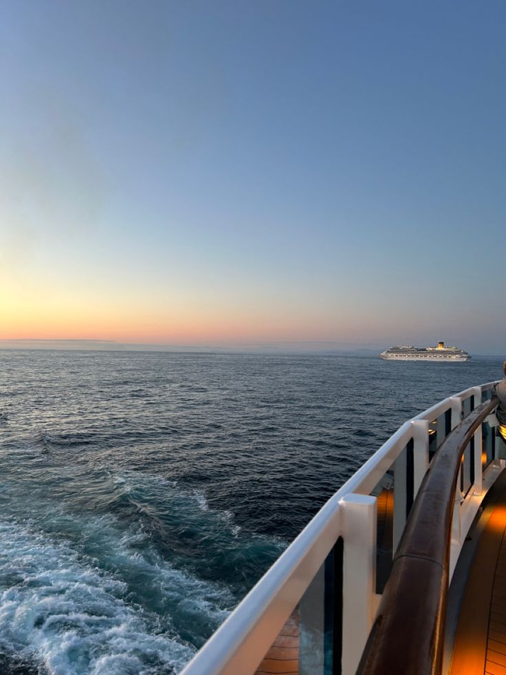 the deck of a cruise ship at sunset with a cruise ship in the distance behind it