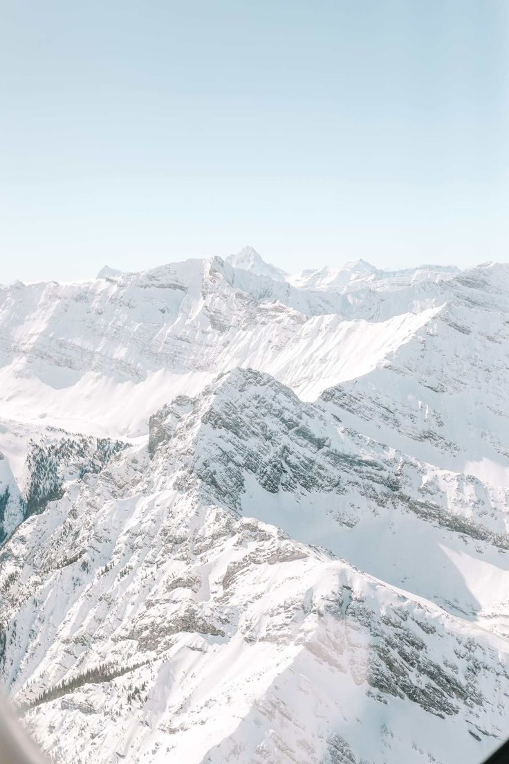 an airplane flying over snow covered mountains under a blue sky