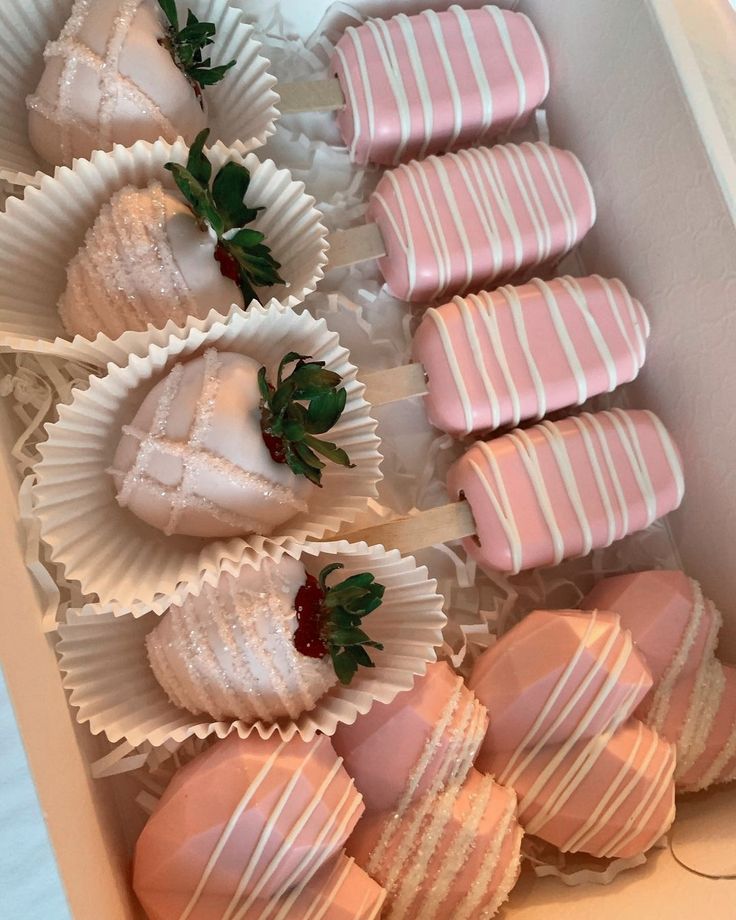 a box filled with pink and white chocolates covered in frosting next to strawberries