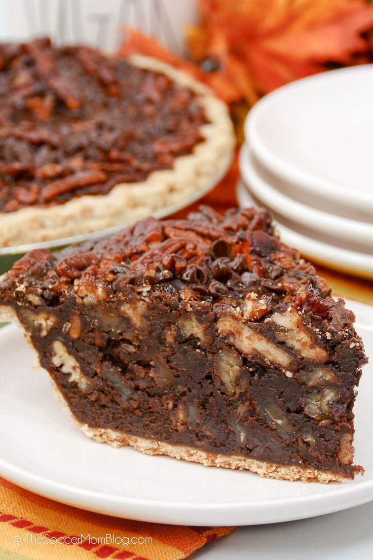 a piece of chocolate pecan pie on a white plate next to plates with autumn leaves