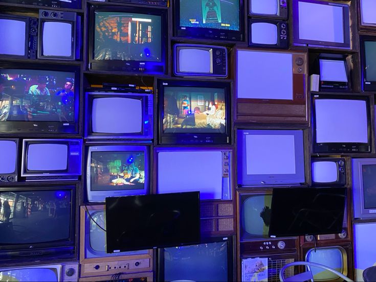 many televisions are stacked on top of each other with blue lights in the background