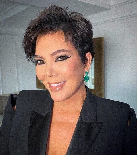 a woman with short hair wearing a black suit and green earrings smiling at the camera