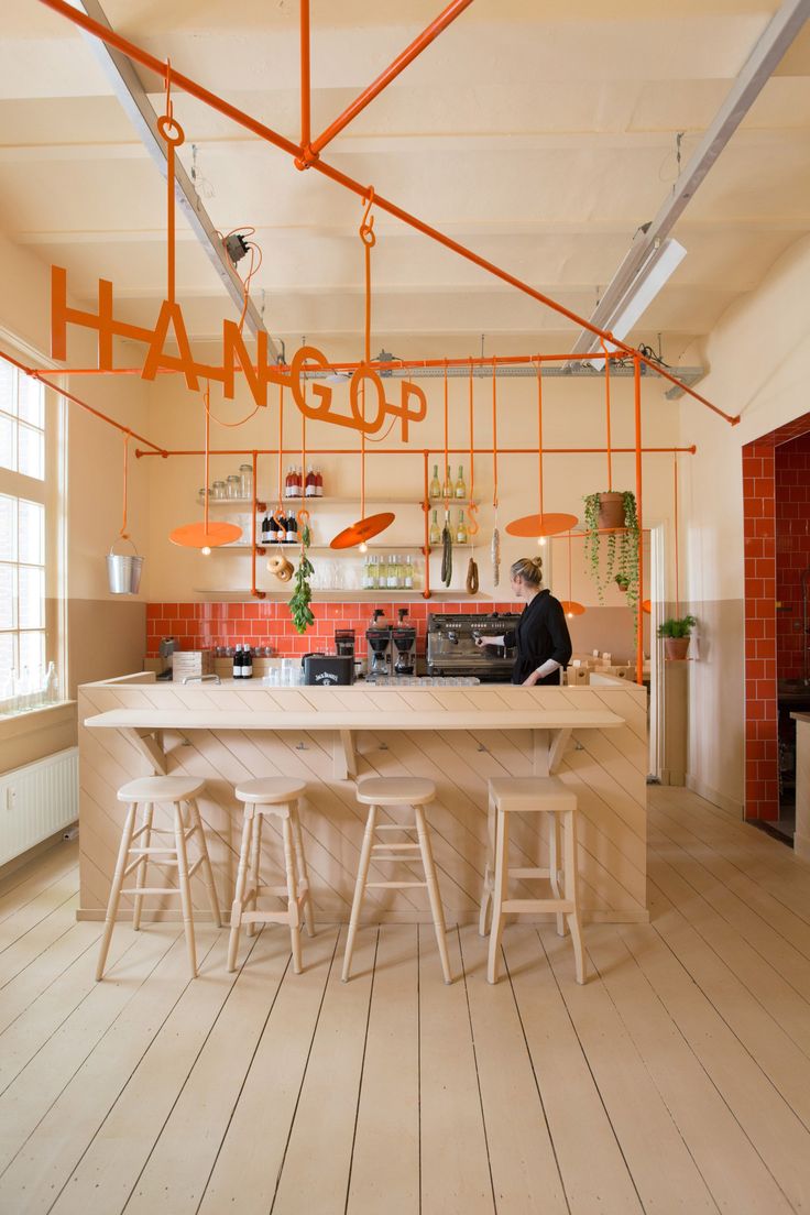 a person sitting at a bar with stools in front of it and an orange sign hanging from the ceiling