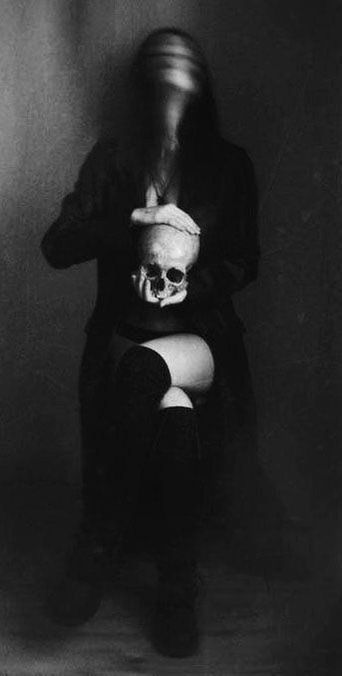 black and white photograph of a woman with a skull on her chest sitting in front of a wall