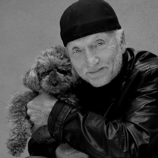 a man holding a dog in his arms while wearing a leather jacket and beanie