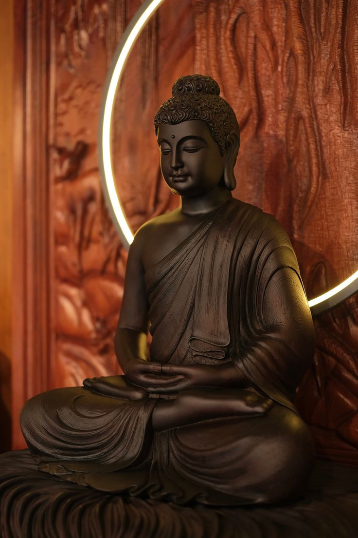 a buddha statue sitting on top of a wooden floor next to a round light fixture