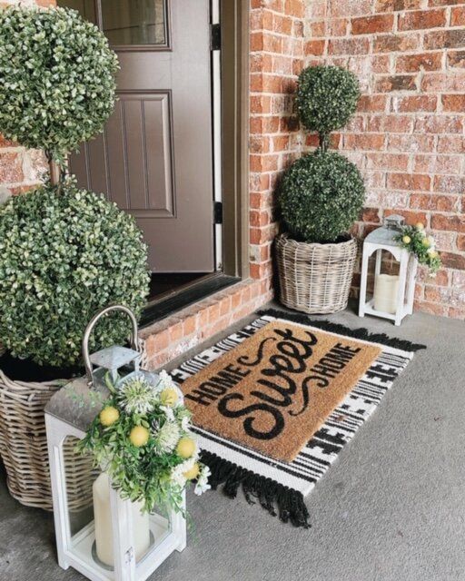 a welcome mat is on the front porch next to two potted plants and a lantern