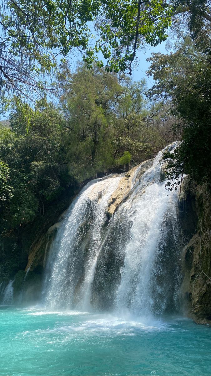 a large waterfall in the middle of a river with blue water and trees around it