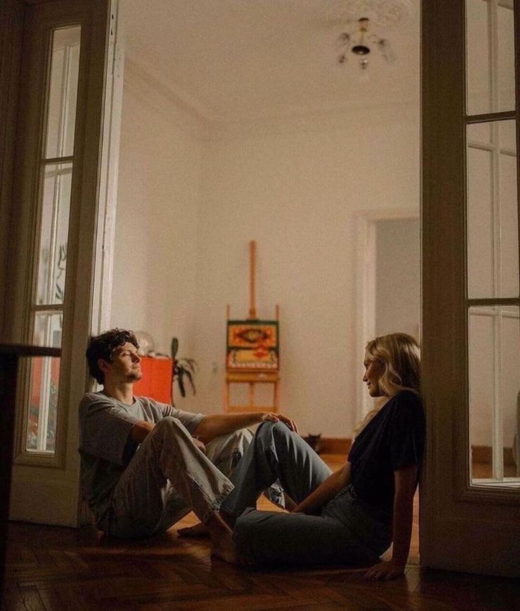 two people sitting on the floor in front of an open door and looking at each other