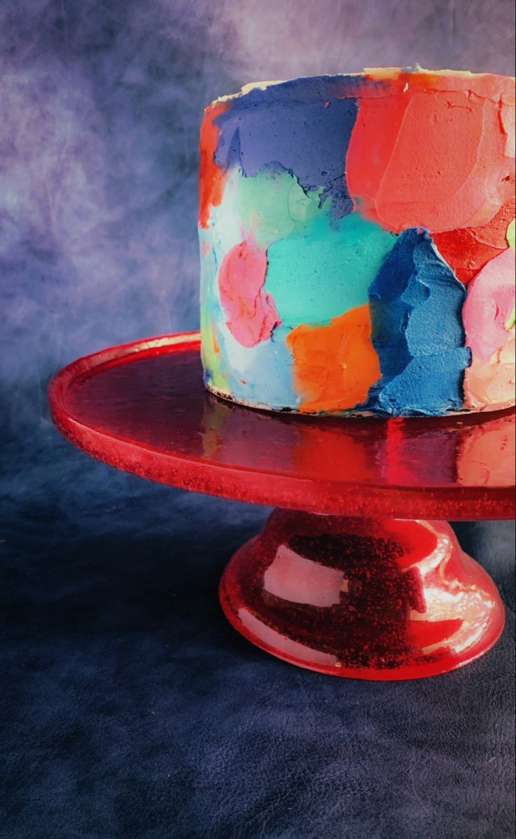 a multicolored cake sitting on top of a red plate next to a blue background