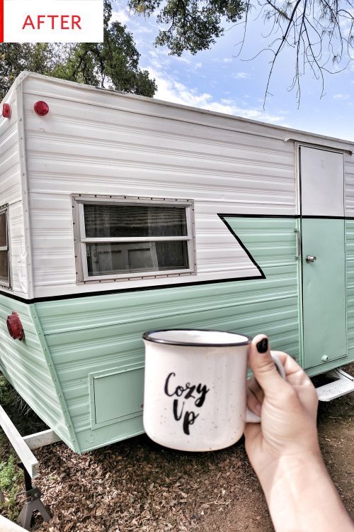 a person holding a paint can next to an old trailer that has been converted into a camper