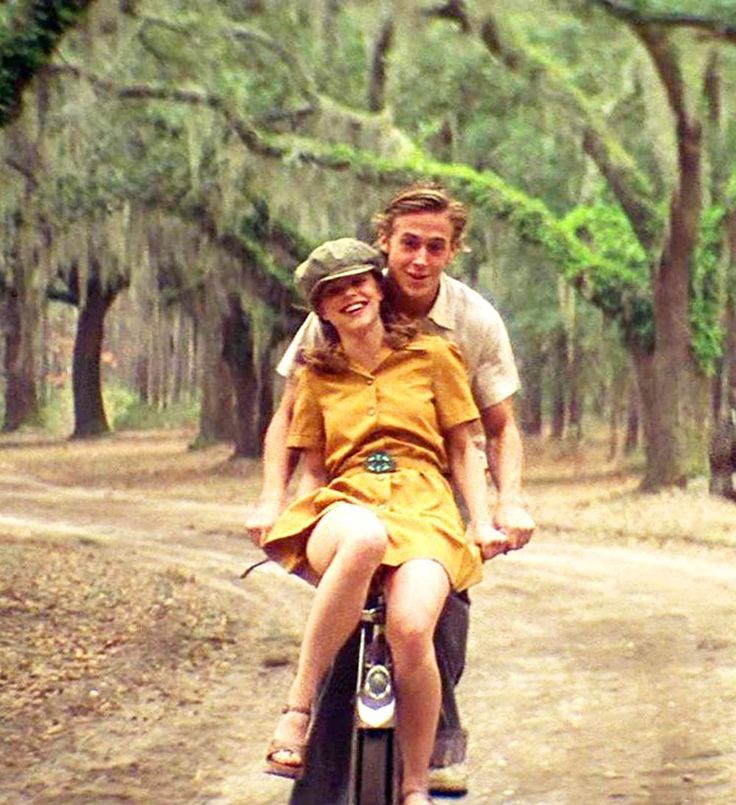 a man and woman riding on the back of a scooter down a dirt road