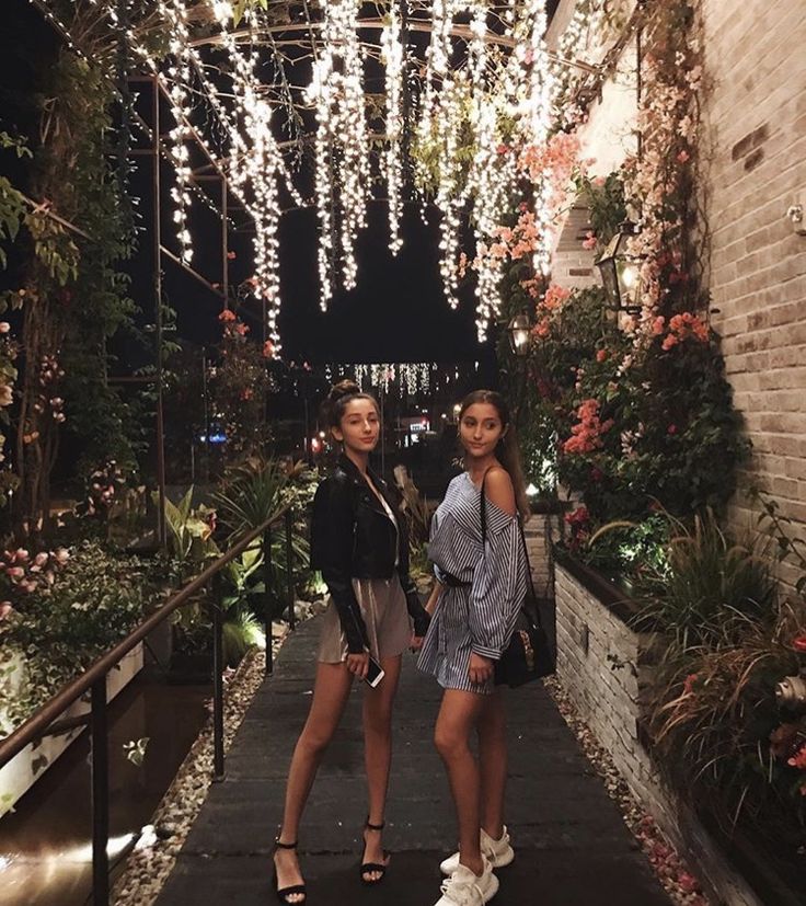 two young women standing in an alleyway with lights strung from the ceiling above them