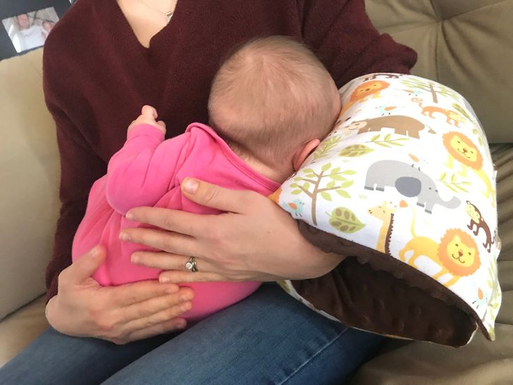 a woman holding a baby in her arms while sitting on a couch next to a pillow