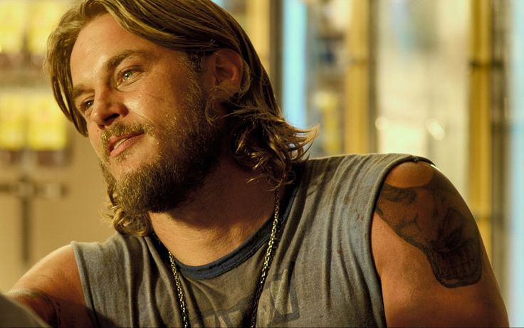 a man with long hair and beard wearing a grey tank top looking off into the distance