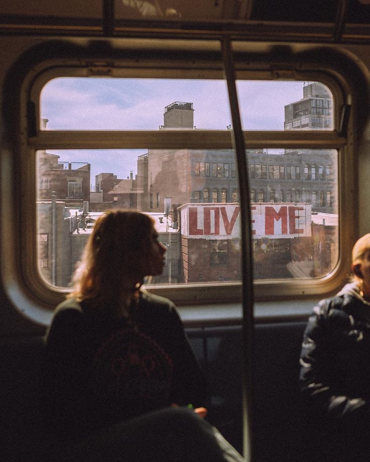 two people sitting on a bus looking out the window with love me written on it