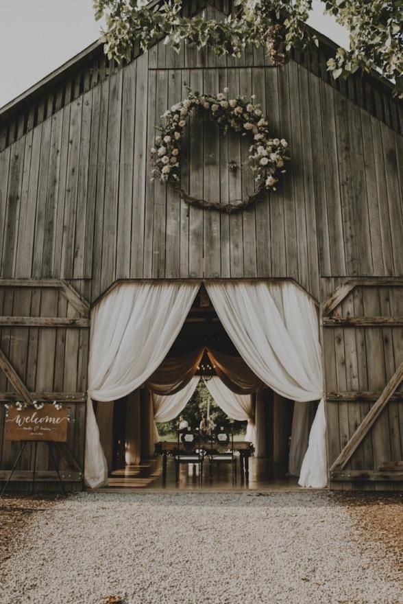 an open barn door with white curtains and flowers on the top, in front of it