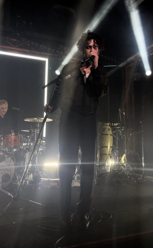 a man singing into a microphone while standing in front of two other men on stage