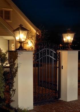 an iron gate is lit up at night in front of a house with two lamps