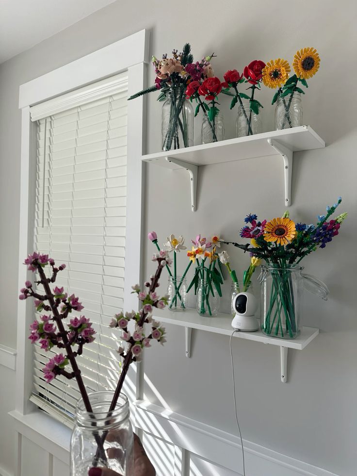 several vases filled with flowers sitting on top of a white shelf next to a window