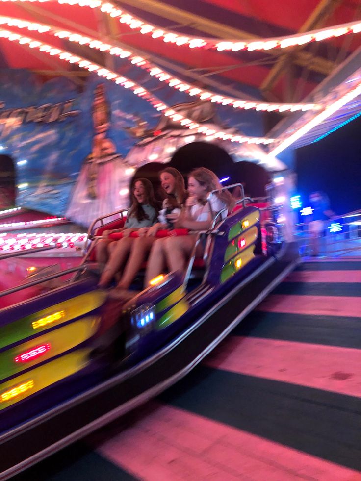 three girls riding on a carnival ride at night