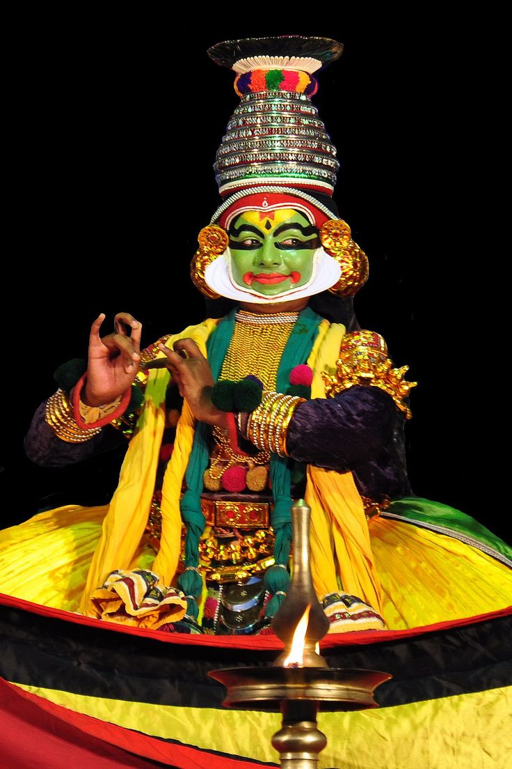 a man dressed in an elaborate costume and holding his hands up to the side while sitting on top of a large object