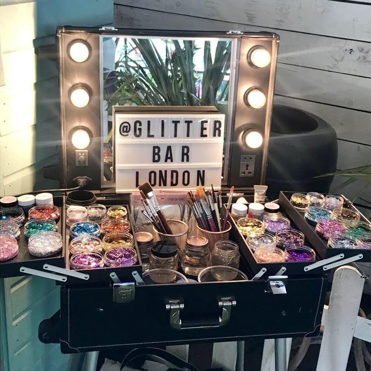 a vanity with lots of makeup products and lights on it's sides, in front of a mirror that says glitter bar london