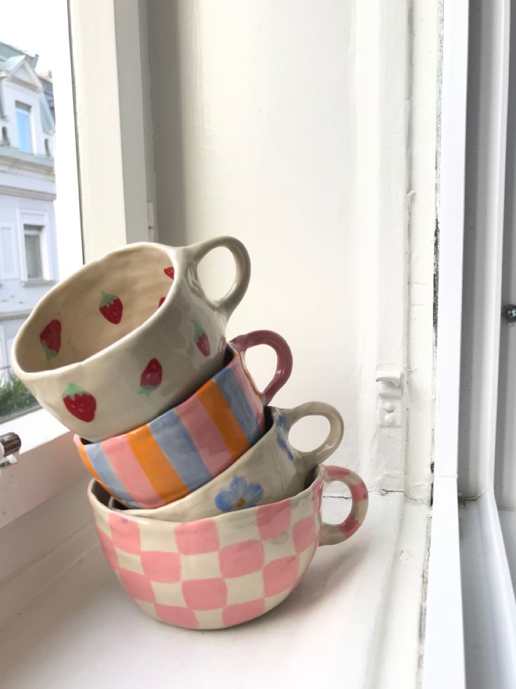 four cups are stacked on top of each other in front of a window sill