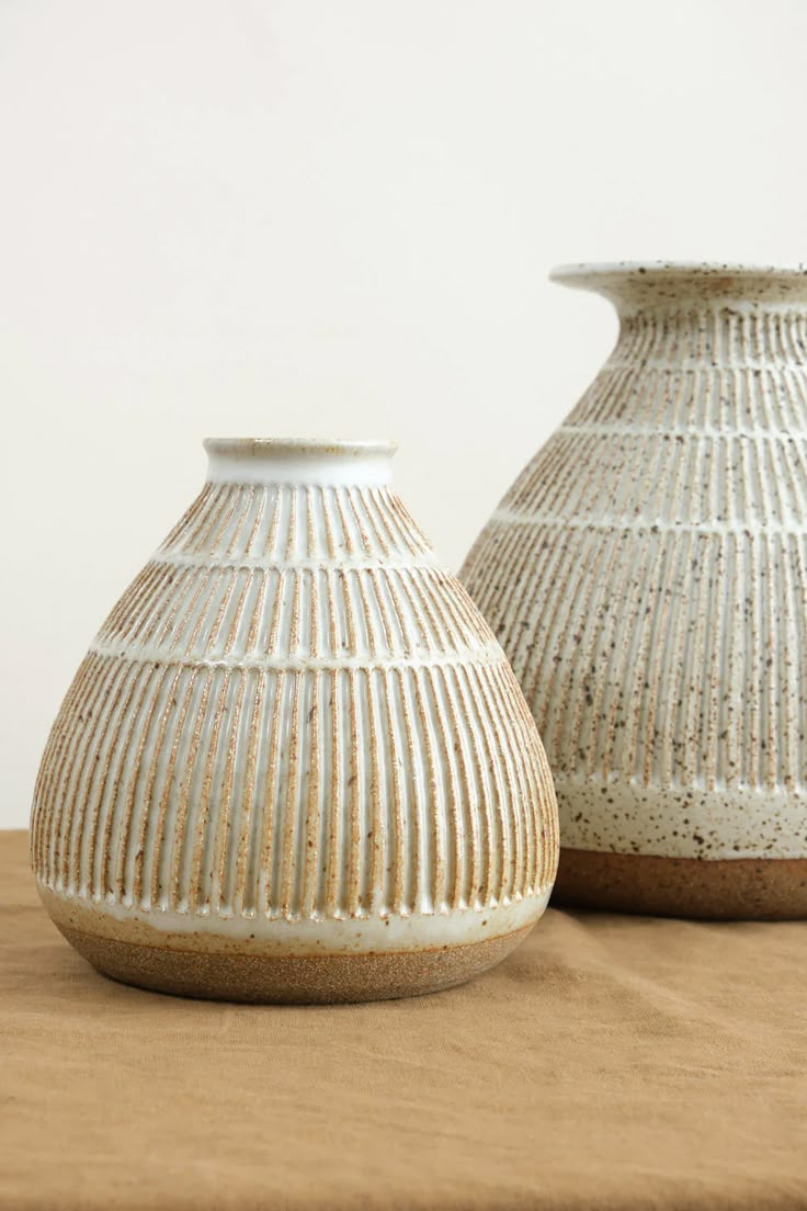 two white vases sitting on top of a wooden table next to eachother