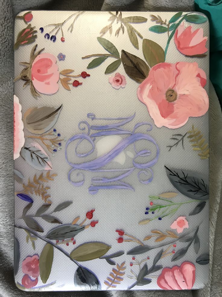 an ipad case with flowers and leaves painted on the front, sitting on a blanket