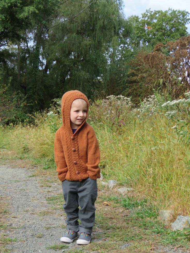 a young boy standing on top of a dirt road next to tall grass and trees