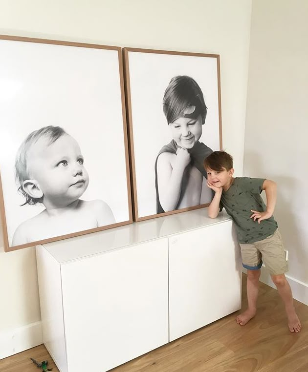 a young boy leaning against a wall with two pictures behind him and his hand on the chest