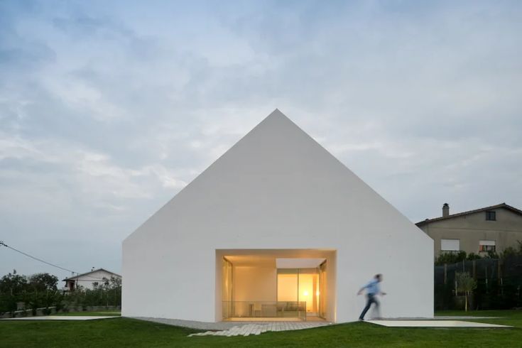 a person walking in front of a white building with a light coming from it's windows