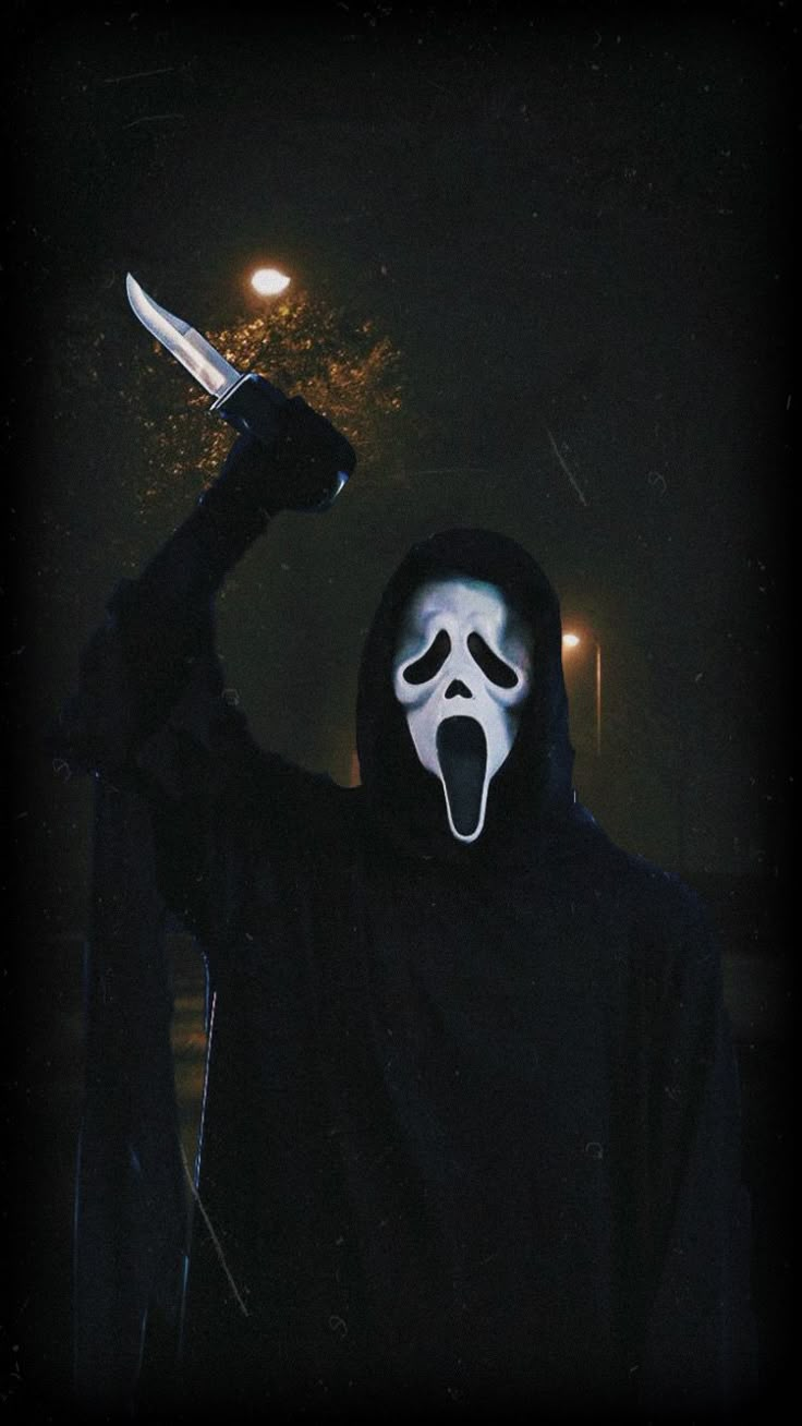 a person wearing a mask and holding a knife in the dark with their face painted white