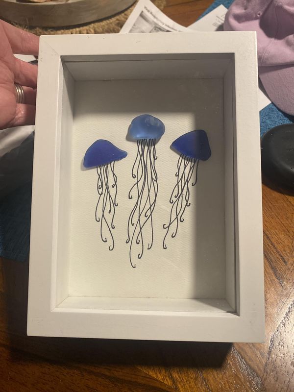 two blue jellyfish in a white frame on a wooden table next to a person's hand