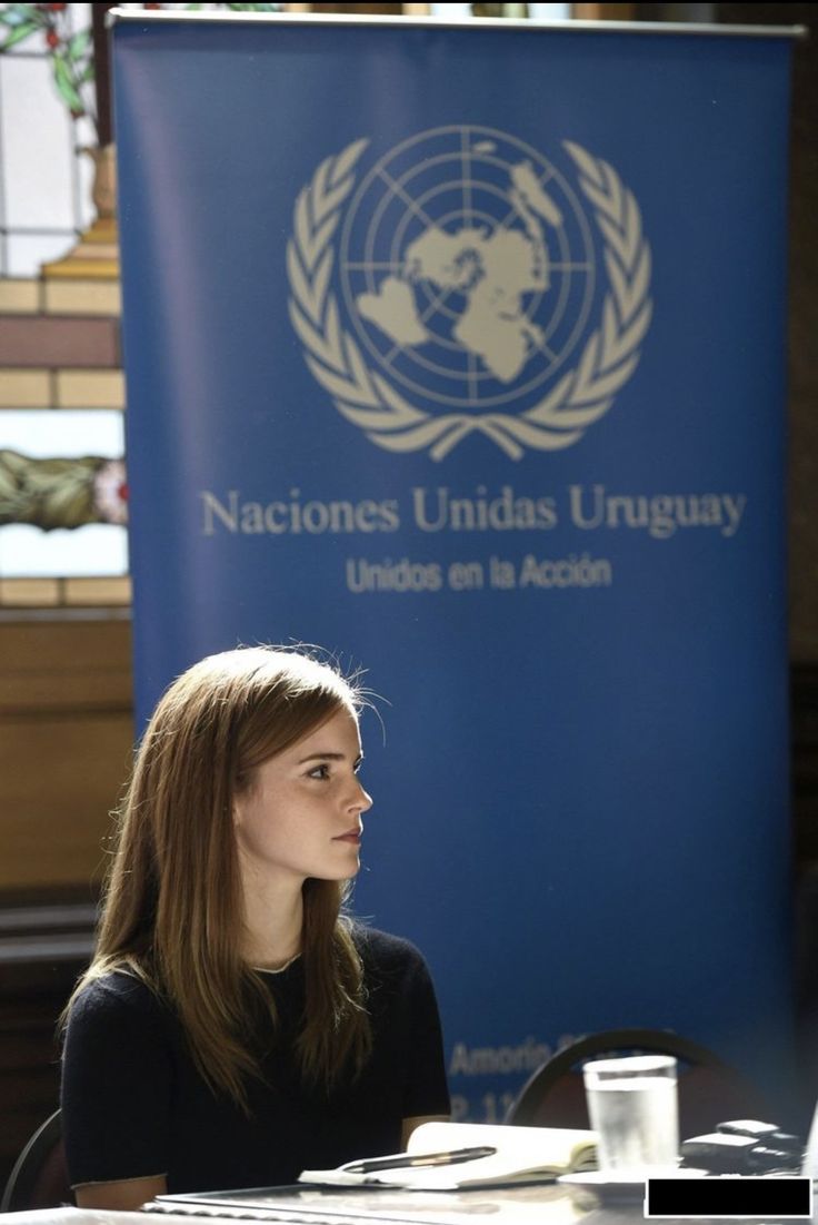 a woman sitting at a table in front of a blue sign with the united nations union logo on it