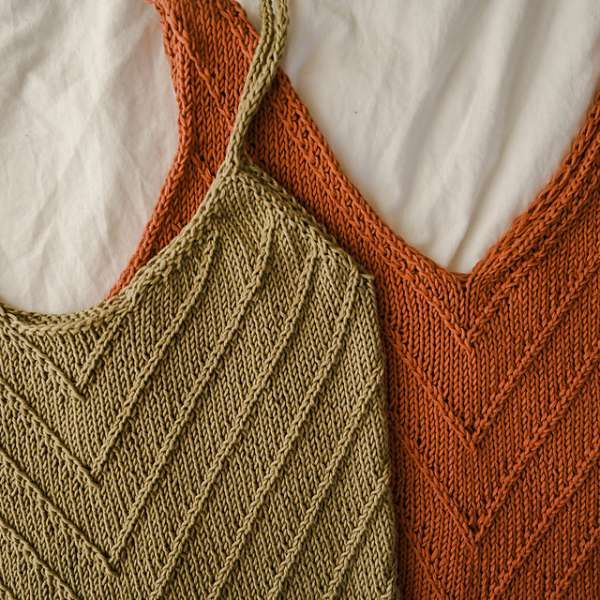 two knitted vests sitting next to each other on top of a white sheet