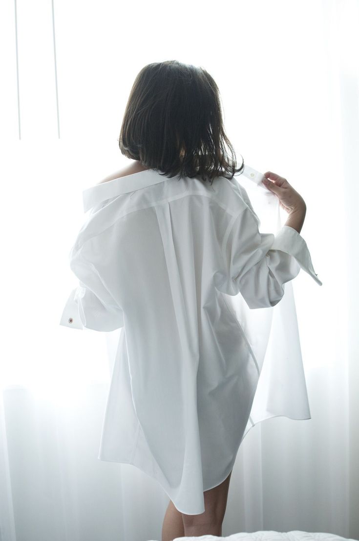 a woman standing in front of a window with her back turned to the camera and holding an object