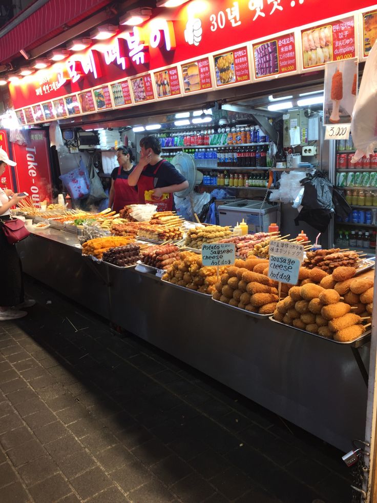 a food stand with lots of different foods on display in front of the counter and people looking at it